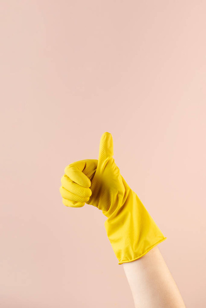 A hand in a yellow rubber glove for washing and cleaning shows a thumbs up. Cleaning concept. - Фото, зображення