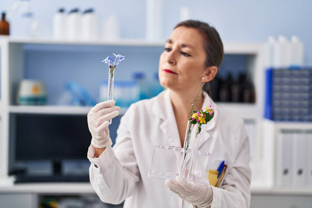 Женщина-ученый средних лет держит в лаборатории пробирки с цветами - Фото, изображение