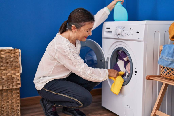 Жінка середнього віку прибирає пральну машинку в пральні
 - Фото, зображення