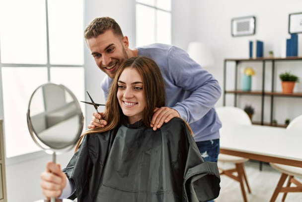 Молодой человек стрижет волосы своей девушке дома. - Фото, изображение