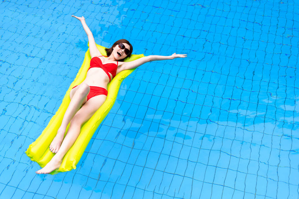 beautiful lady in sexy red bikini swims in a luxury hotel pool on an inflatable mattress - 写真・画像