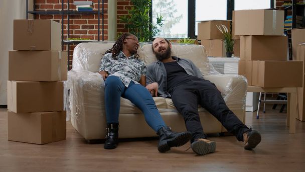 Casal multiétnico relaxante no sofá depois de desembalar móveis - Foto, Imagem