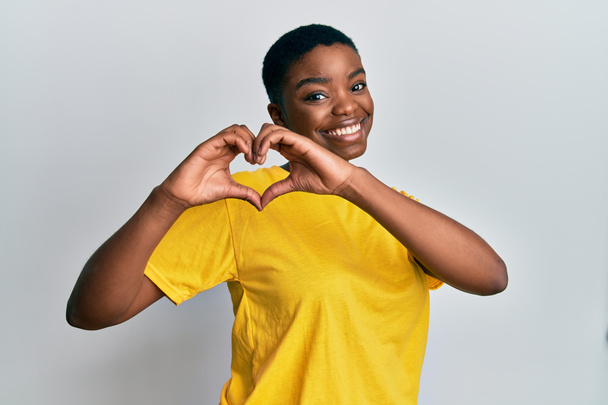 Jonge Afro-Amerikaanse vrouw draagt casual geel t-shirt glimlachend in liefde doet hart symbool vorm met handen. romantisch concept.  - Foto, afbeelding