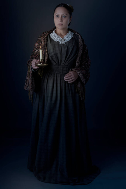 A Victorian working class woman standing alone holding a candle in the dark - Foto, imagen