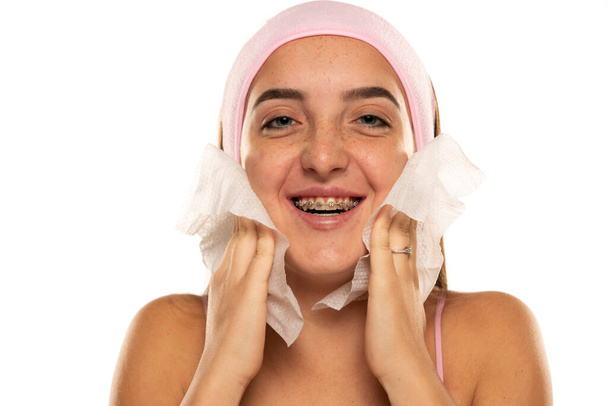 young happy woman with headband cleans her face with wet wipes on white background. - Photo, image