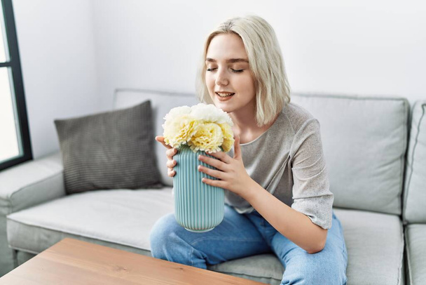 Молодая белая женщина улыбается уверенно пахнущие цветы дома - Фото, изображение