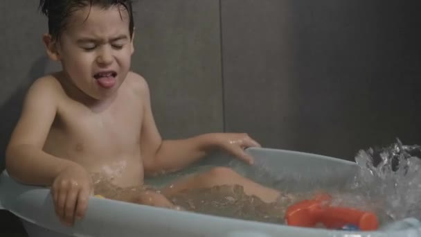 Kaukázusi fiú szórakozik, vizet fröcsköl és mosolyog fürdés közben a fürdőszobában. Fürdőszobai higiénia. Gyönyörű portré az életmód design. Egészséges. - Felvétel, videó