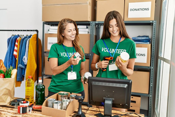 Moeder en dochter dragen vrijwilliger uniform scannen voedsel met behulp van barcode lezer in het liefdadigheidscentrum - Foto, afbeelding