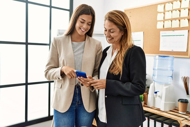 Äiti ja tytär yritystyöntekijät hymyilevät luottavaisesti käyttämällä älypuhelinta toimistossa - Valokuva, kuva
