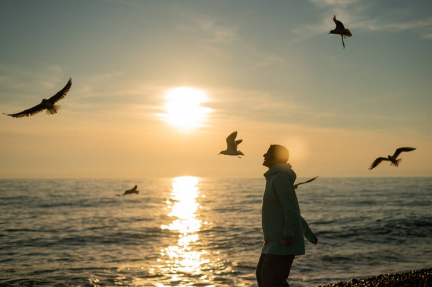 Caucasian woman feeding seagulls at sunset by the sea.  - Photo, image