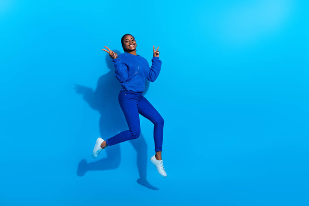 Photo of excited shiny woman wear sweatshirt jumping showing v-sign empty space isolated blue color background - Foto, Imagem