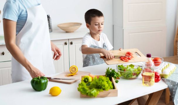 Self-dependent child unaided is cooking salad mixing ingredients of bowl at kittchen. Healthy food concept. - Photo, Image