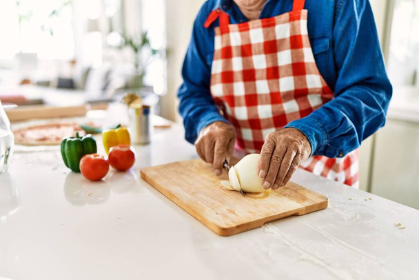 Senior man snijden ui in de keuken - Foto, afbeelding
