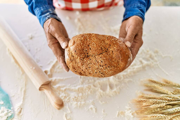 Senior man holding wholemeal bread at kitchen - Fotó, kép