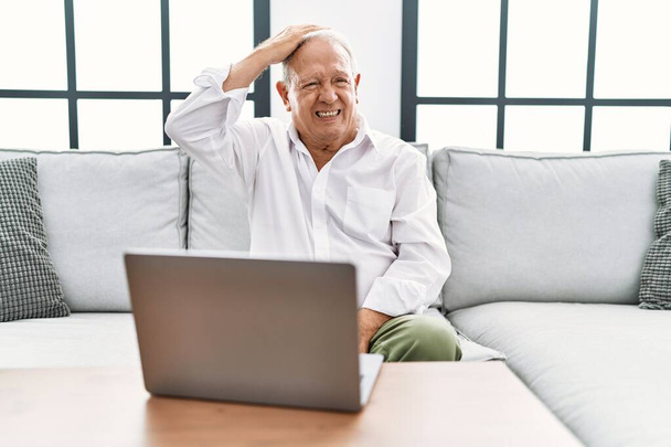 Senior man using laptop at home sitting on the sofa confuse and wonder about question. uncertain with doubt, thinking with hand on head. pensive concept.  - Φωτογραφία, εικόνα