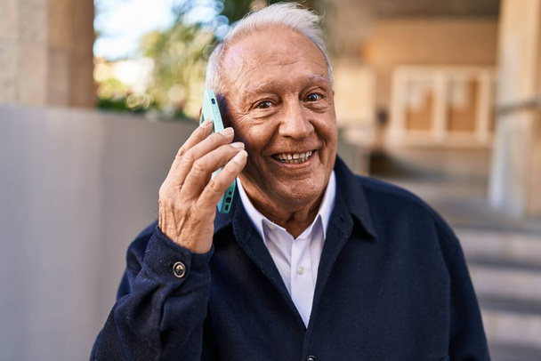 Старший чоловік посміхається впевнено розмовляє по смартфону на вулиці
 - Фото, зображення