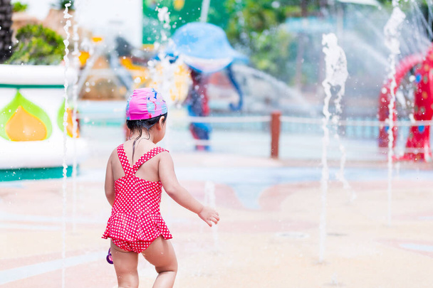 Позаду чорний вид. Портрет 3-4 років. Азійська дівчинка грає у фонтан подвір'я. У літній час. Парень в красном плавании. Яскравість у дитинстві. Діяльність з жаркою погодою. Копіювальний простір - Фото, зображення