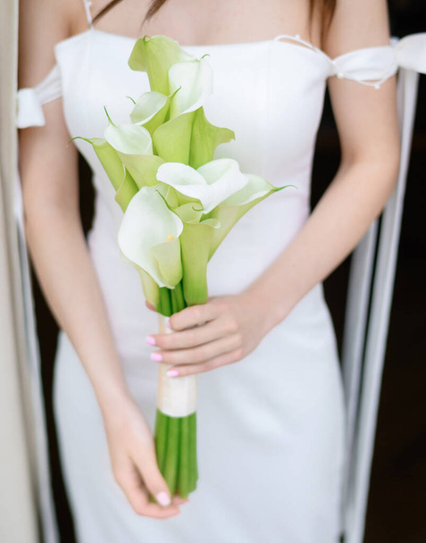 Beautiful young bride posing with a bouquet in her hands by the window - Foto, imagen