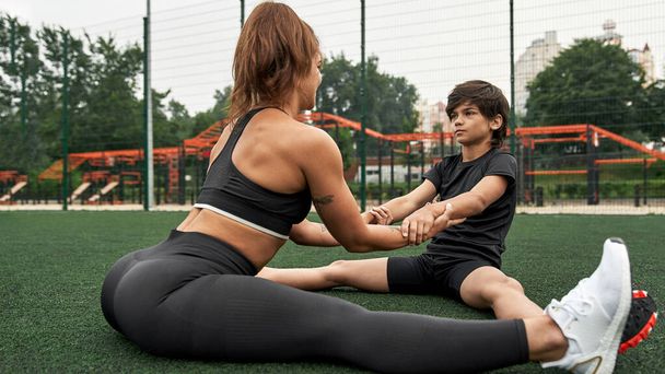 Athletic mother and son warm up on athletic field - Фото, изображение