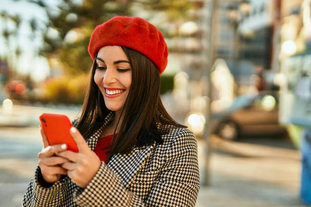 Giovane donna ispanica sorridente felice utilizzando smartphone in città. - Foto, immagini