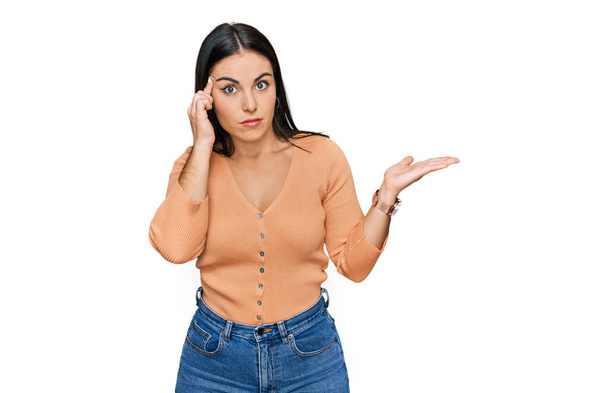 Mujer hispana joven vestida con ropa casual confundida y molesta con la palma abierta mostrando espacio para copiar y señalando con el dedo a la frente. Piénsalo.  - Foto, Imagen