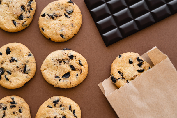Top view of cookies, paper bag and chocolate bar on brown background  - Fotó, kép
