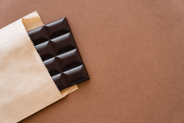 Vista superior de la barra de chocolate negro en paquete de artesanía sobre fondo marrón  - Foto, imagen