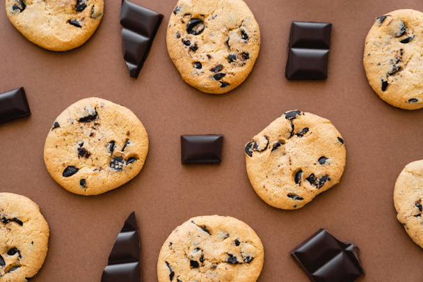 Top view of chocolate pieces near cookies on brown background  - Fotó, kép