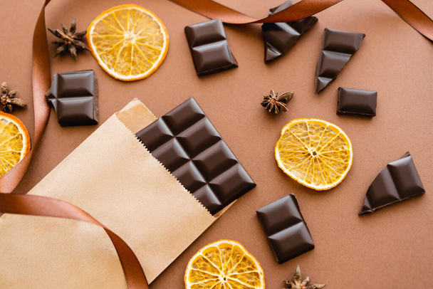 Top view of anise, dry orange slices and chocolate on craft package with ribbon on brown background  - Фото, зображення