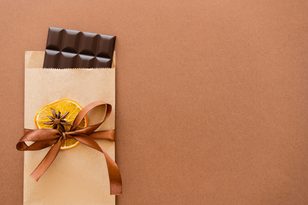 Вид зверху шоколаду в крафтовій упаковці з апельсиновим скибочкою та анісом на коричневому фоні
  - Фото, зображення