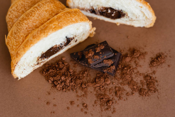Top view of chocolate and dry cocoa near croissant on brown background  - Foto, immagini