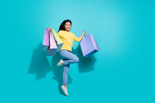 Full length photo of excited sweet lady dressed yellow sweater jumping holding shoppers empty space isolated turquoise color background - Foto, immagini