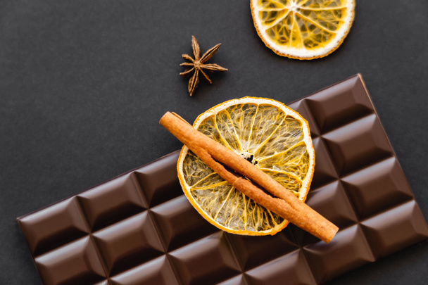 Top view of cinnamon on dry orange slice and chocolate bar on black background - Фото, зображення