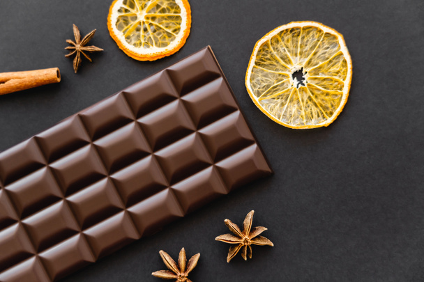 Top view of chocolate bar near dry orange slices and anise on black background - Fotó, kép