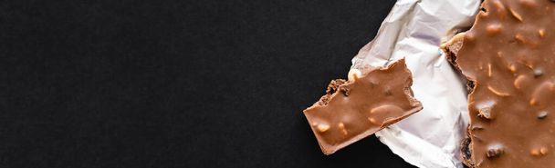 Top view of milk chocolate with nuts on foil on black background, banner  - Photo, Image