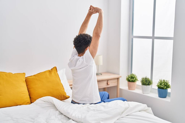 Hombre árabe joven despertando estirando los brazos en el dormitorio - Foto, imagen