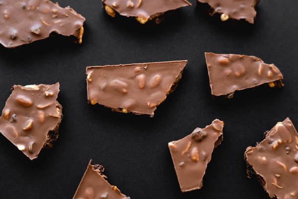Vista superior de piezas de chocolate con leche con nueces sobre fondo negro - Foto, imagen