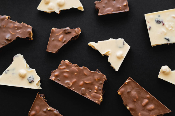 Top view of pieces of milk and white chocolate on black background - Φωτογραφία, εικόνα