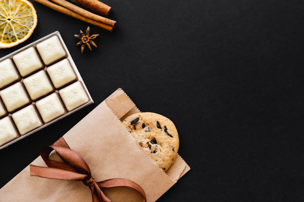 Top view of cookie in craft package, chocolate and dry spices on black surface  - 写真・画像