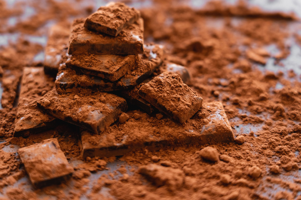 Vue rapprochée du cacao en poudre et du chocolat noir sur fond noir  - Photo, image