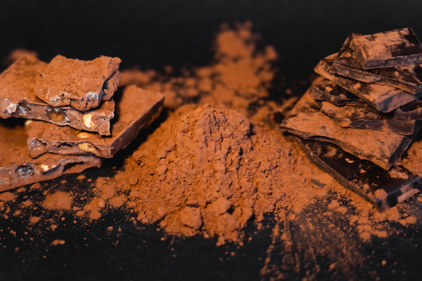 Vista de cerca del cacao natural en polvo y chocolate sobre fondo negro  - Foto, imagen