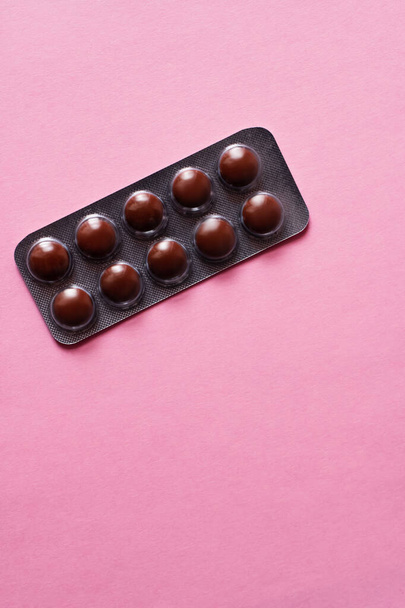 bovenaanzicht van blisterverpakking met donkere pillen geïsoleerd op roze - Foto, afbeelding
