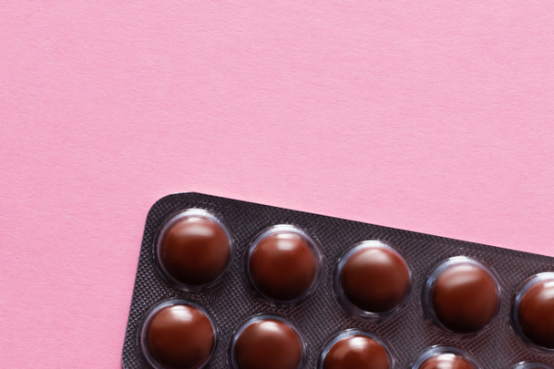 close up view of blister pack with dark brown pills isolated on pink - Foto, afbeelding