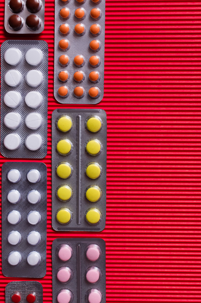 top view of blister packs with different pills on crimson textured background  - 写真・画像