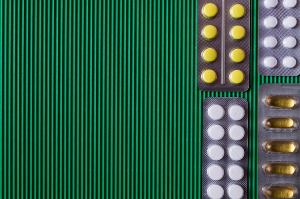 bovenaanzicht van blisterverpakkingen met verschillende pillen en capsules op gestructureerde groene achtergrond - Foto, afbeelding