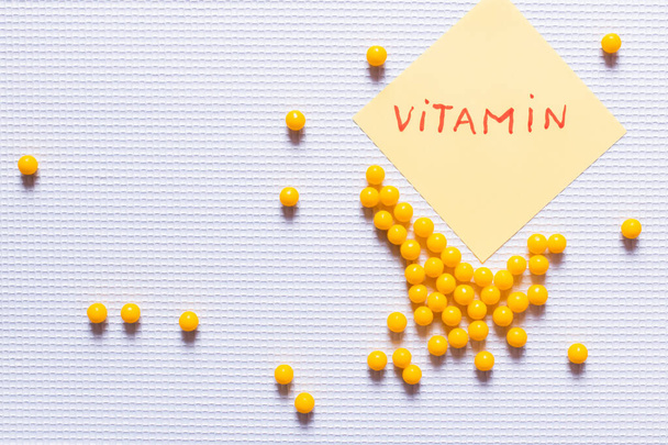 vista superior de la medicación de forma redonda amarilla cerca de la nota de papel con letras de vitaminas sobre fondo texturizado blanco - Foto, imagen