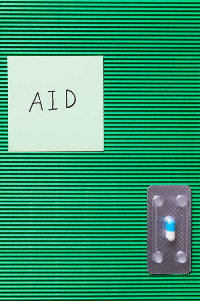 vista superior del blister con la píldora cerca de la nota de papel con letras de ayuda sobre fondo verde texturizado - Foto, Imagen