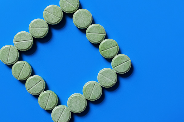 top view of green pills in shape of rhombus on bright blue background - Foto, Imagem