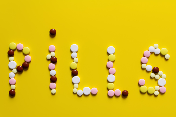 top view of pills word made of colorful round shape medication on yellow background - Zdjęcie, obraz