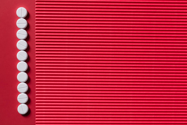 top view of vertical row with white round shape pills on crimson and textured background - Valokuva, kuva